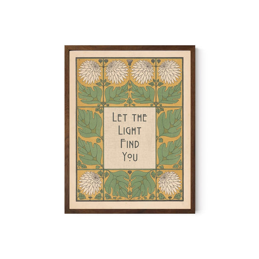 May include: Framed art print with a botanical design. The artwork features a central text box with the words "Let the Light Find You" in a stylized font. The border includes green leaves, white flowers, and a yellow background. The frame is a dark brown color.
